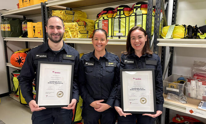 Two Leidos Australia Mission Aircrew holding Certificates, standing alongside Leidos RTO Compliance and Development Manager Nicole Powell