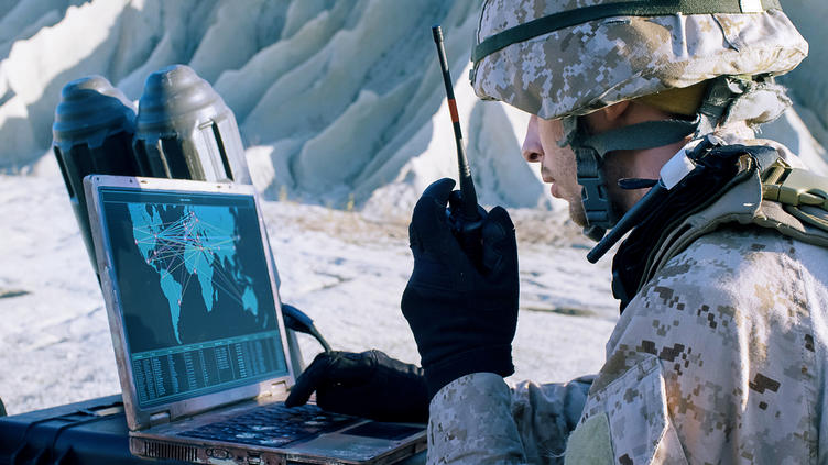 Solider in front of laptop with walkie talkie