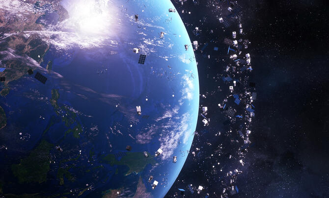 Earth is shown from space surrounded by a dense cloud of satellites and debris orbiting the planet. The scene highlights the crowded environment in Earth’s orbit against a dark starry background.