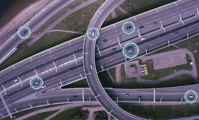Aerial view of a highway interchange with digital overlays highlighting connected vehicles, illustrating intelligent transportation systems, real-time traffic monitoring, and vehicle-to-infrastructure communication.