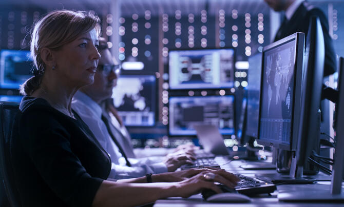 Cybersecurity analysts monitor network activity from a security operations center, using multiple screens displaying maps, dashboards, and threat data to detect and respond to potential cyber threats.