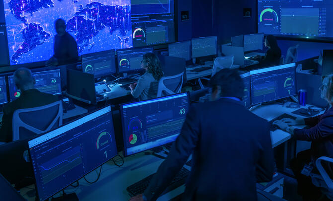 Cyber operations center with analysts monitoring multiple dashboards and global network activity across large display walls, supporting real-time cybersecurity monitoring and threat detection.
