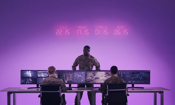 Military personnel monitor geospatial imagery and data across multiple screens in an operations center, illustrating the use of AI-enabled analysis for situational awareness.