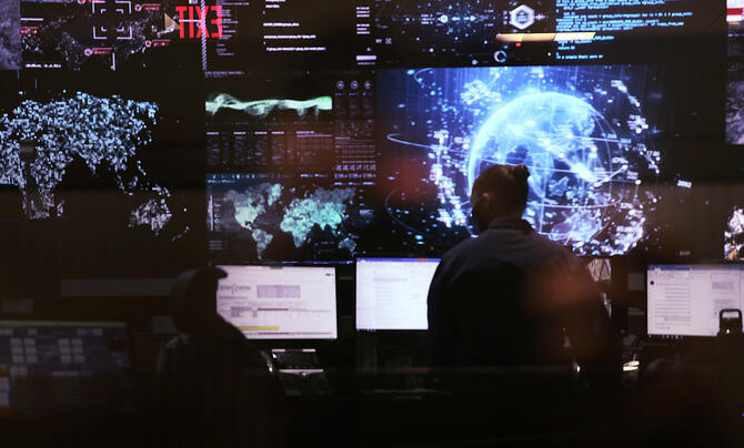 A person facing away toward many screens showing the earth and the globe and other data