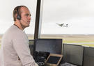 Side view of young man in air traffic control tower, looking away, airplane taking off behind