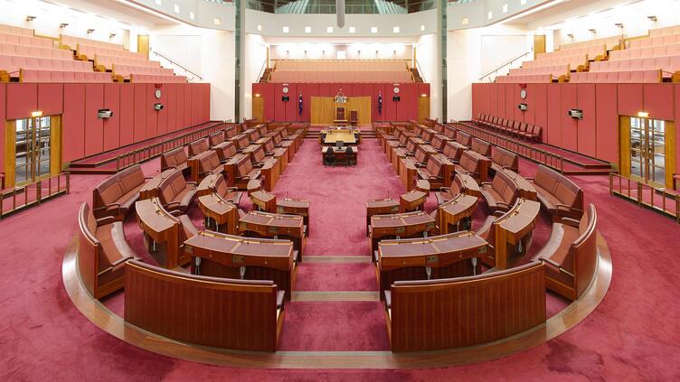 A photo of the senate part of parliament house with a semicircle of chairs facing a single chair. Everything is red